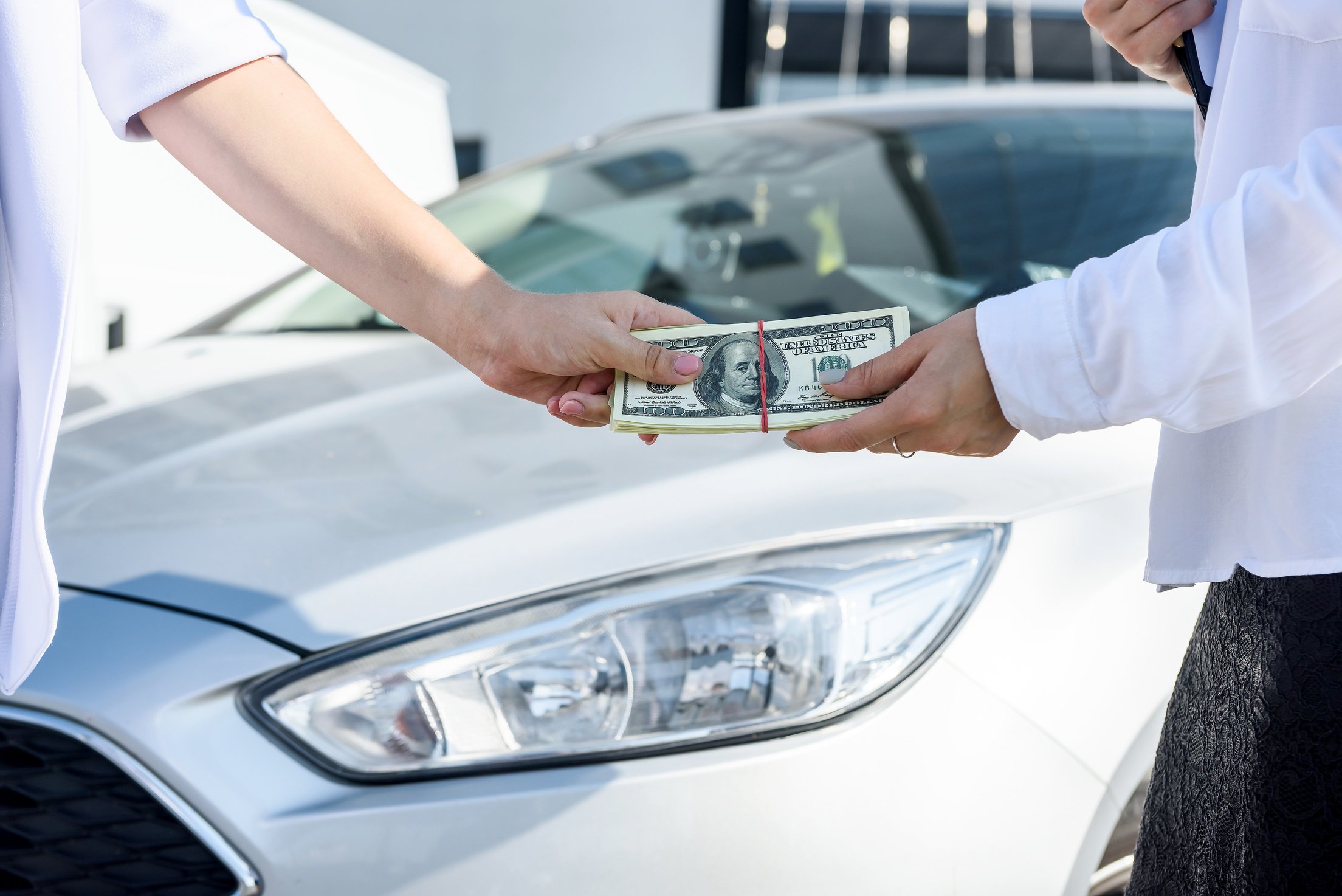 Hands with Dollar Bundle over Car Hood. Car Sale or Car Rental Concept